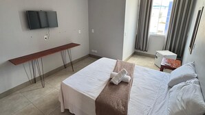 Una camera d'albergo con un letto, una scrivania, una TV a parete e una finestra con tende.