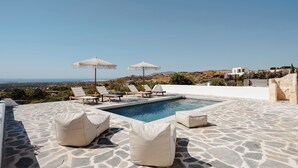 Zona de piscina con suelo de piedra, sillas de descanso y sombrillas.