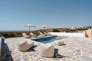 A pool area with stone flooring, lounge chairs, and umbrellas. - Villa THÉA III, Villa THÉA Naxos (Naxos)