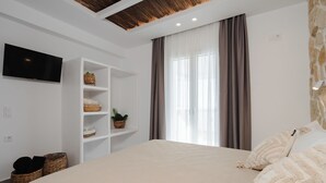 Un dormitorio con una cama grande, un televisor en la pared, un estante con cestas y una ventana con cortinas.