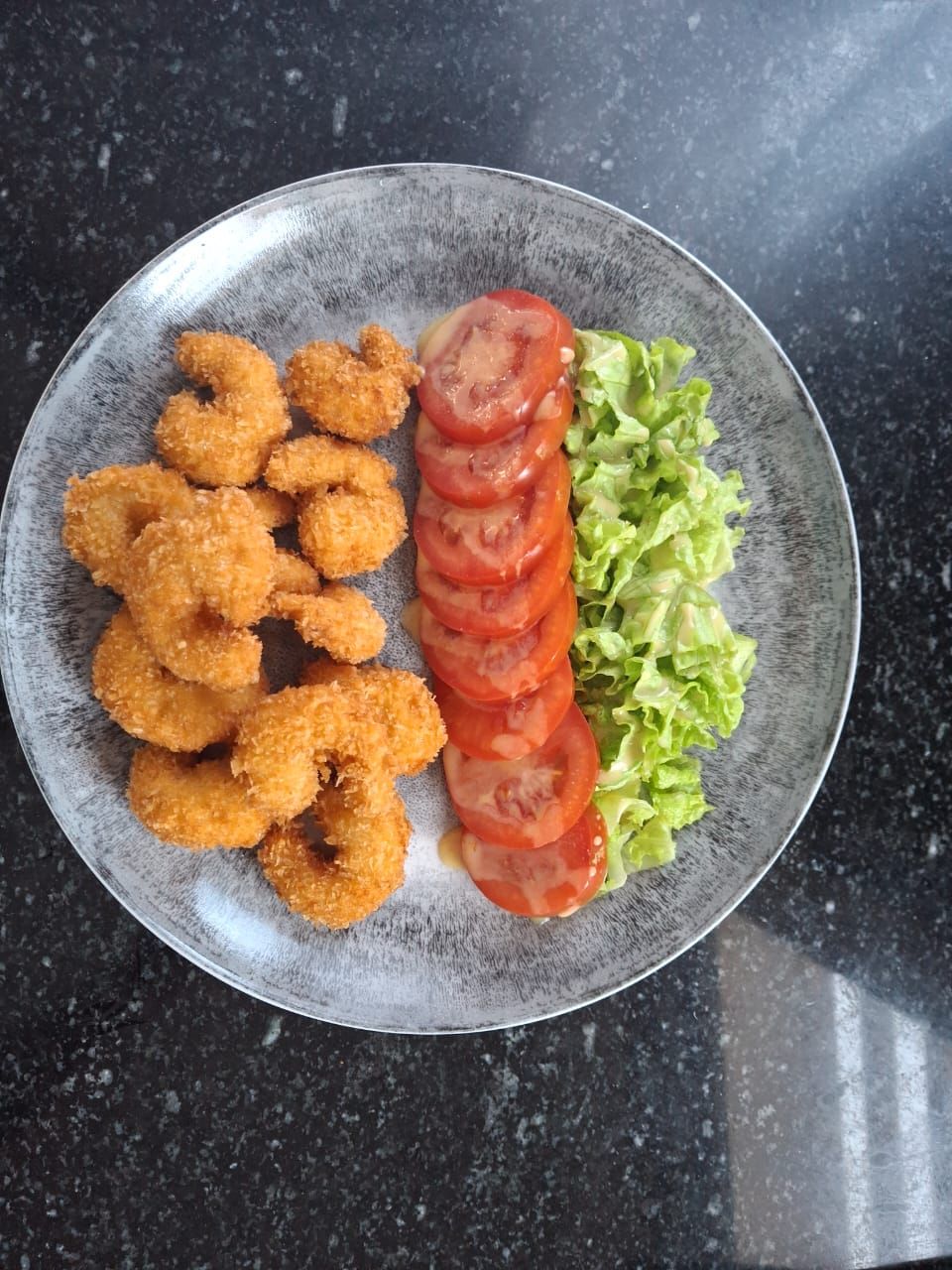 A plate with fried food, sliced tomatoes, and lettuce.