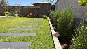 A well-maintained garden with a stone pathway, a seating area with chairs and an umbrella, and a high wall with barbed wire. - Tia Vahine - Boutique Hôtel Ivato (Antananarivo)