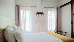A bedroom with a large bed, a wooden headboard, a bedside table, and a window with curtains. - Tia Vahine - Boutique Hôtel Ivato (Antananarivo)