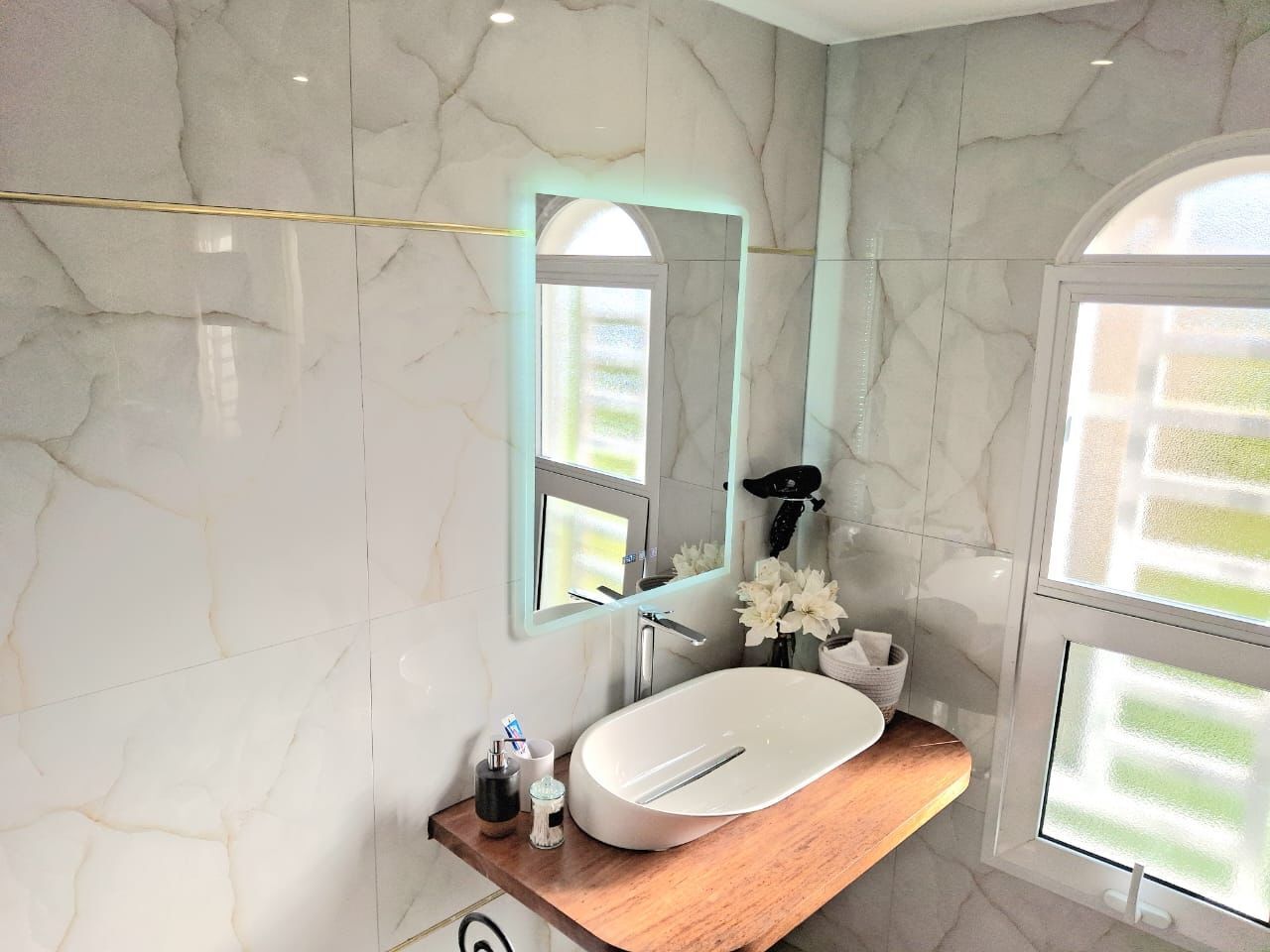Een moderne badkamer met een marmeren wand, een houten wastafelmeubel, een witte wasbak en een grote spiegel.