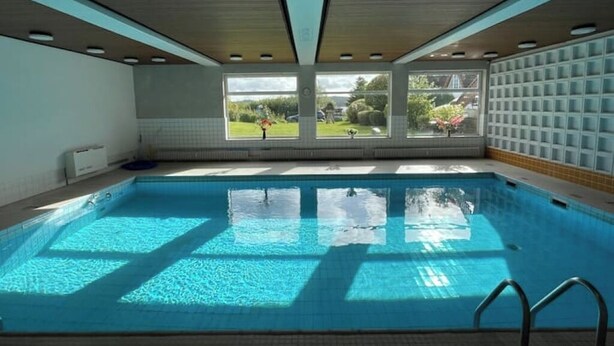 En swimmingpool med udsigt til en have gennem store vinduer.