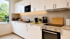 A modern kitchen with white cabinets, a microwave, an oven, and a window with a view of greenery. - House Deichlust Whg.1,Strichweg 165, 27476 Cuxhaven-Döse (Cuxhaven-Döse)