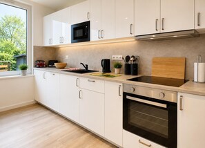 A modern kitchen with white cabinets, a microwave, an oven, and a window with a view of greenery. - House Deichlust Whg.1,Strichweg 165, 27476 Cuxhaven-Döse (Cuxhaven-Döse)