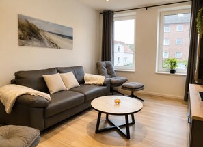 Un salon moderne avec un canapé en cuir, une table basse ronde et une vue sur un immeuble par la fenêtre.
