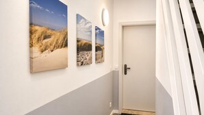 Ein Flur mit einer weißen Tür, einer schwarzen Fußmatte und drei Landschaftsbildern an der Wand.