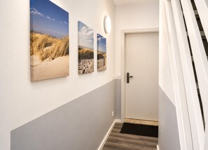 A hallway with a white door, a black doormat, and three landscape paintings on the wall. - House Deichlust Whg.1,Strichweg 165, 27476 Cuxhaven-Döse (Cuxhaven-Döse)