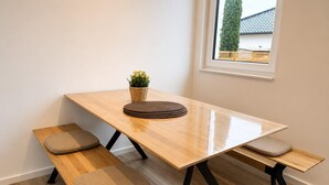A wooden dining table with benches, a small potted plant, and a window with a view of a house. - House Deichlust Whg.1,Strichweg 165, 27476 Cuxhaven-Döse (Cuxhaven-Döse)