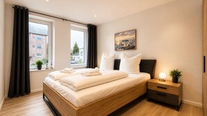 Ein modernes Schlafzimmer mit einem hölzernen Bett, einem Nachttisch mit Lampe und Blick ins Freie.