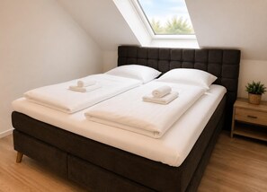 A bed with a dark headboard, white linens, and a skylight above. - House Deichlust Whg.3,Strichweg 165, 27476 Cuxhaven-Döse (Cuxhaven-Döse)