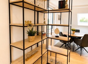 A modern interior with a multi-tiered wooden shelving unit, a dining table with chairs, and a window providing natural light. - House Deichlust Whg.3,Strichweg 165, 27476 Cuxhaven-Döse (Cuxhaven-Döse)