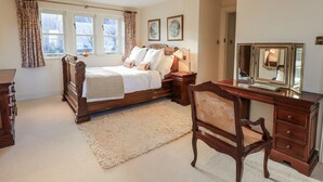 A bedroom with a large bed, a wooden desk, a chair, and a dresser. There are three windows with curtains, a rug on the floor, and a framed picture on the wall. - Orchard House (Leyburn)