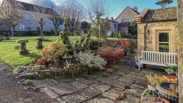 A stone pathway leading to a bench in a garden with stone planters and a stone wall. - Orchard House (Leyburn)