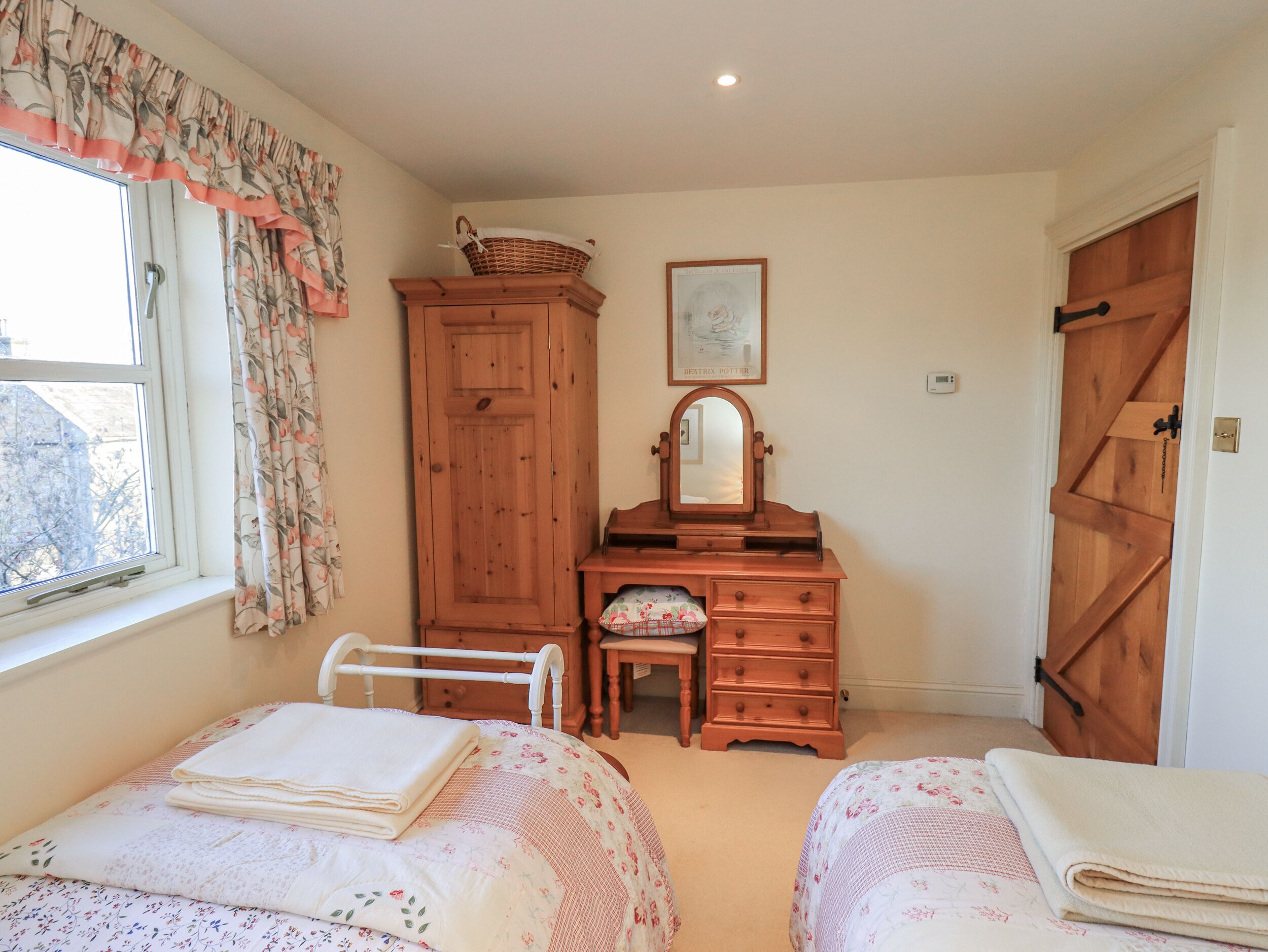 A bedroom with two beds, a wooden dresser, a mirror, and a window with floral curtains.