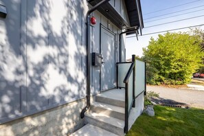 A modern building with a garage door, a mailbox, and a set of concrete steps leading to a glass door. - Sunny 1BR Detached Suite • Near City Center (Vancouver)