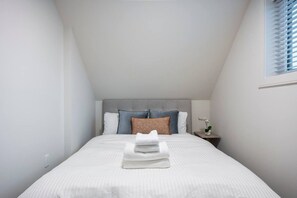 Un dormitorio con una cama, almohadas, una mesita de noche con una planta y una ventana con persianas.