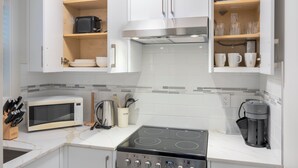 A modern kitchen with white cabinets, a microwave, a stove, and various kitchen utensils. - Soothing 1-bedroom condo with AC in vibrant Vancouver (Vancouver)
