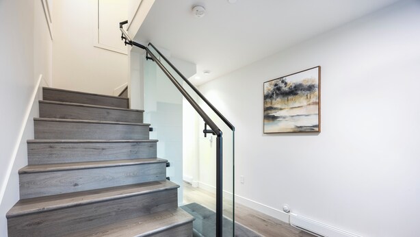 A staircase with wooden steps and a glass railing, leading to a room with a painting on the wall. - Soothing 1-bedroom condo with AC in vibrant Vancouver (Vancouver)