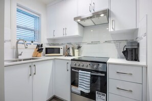 Una cocina moderna con armarios blancos, una campana extractora de acero inoxidable, un microondas, una cafetera y una estufa a gas.