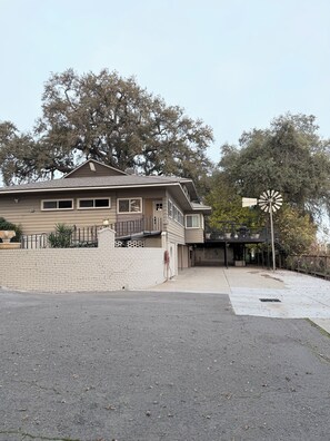 A two-story house with a brick wall, a windmill, and a large tree in the background. - Spacious Riverfront Getaway 5 beds 3.5 bath & views (Sacramento)
