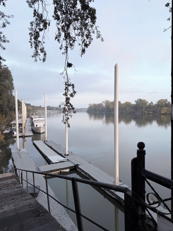 A dock with boats, a calm lake, and trees in the background. - Spacious Riverfront Getaway 5 beds 3.5 bath & views (Sacramento)