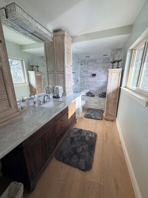 A bathroom with a large mirror, wooden cabinets, a marble countertop, a shower with a glass door, and a window. - Spacious Riverfront Getaway 5 beds 3.5 bath & views (Sacramento)