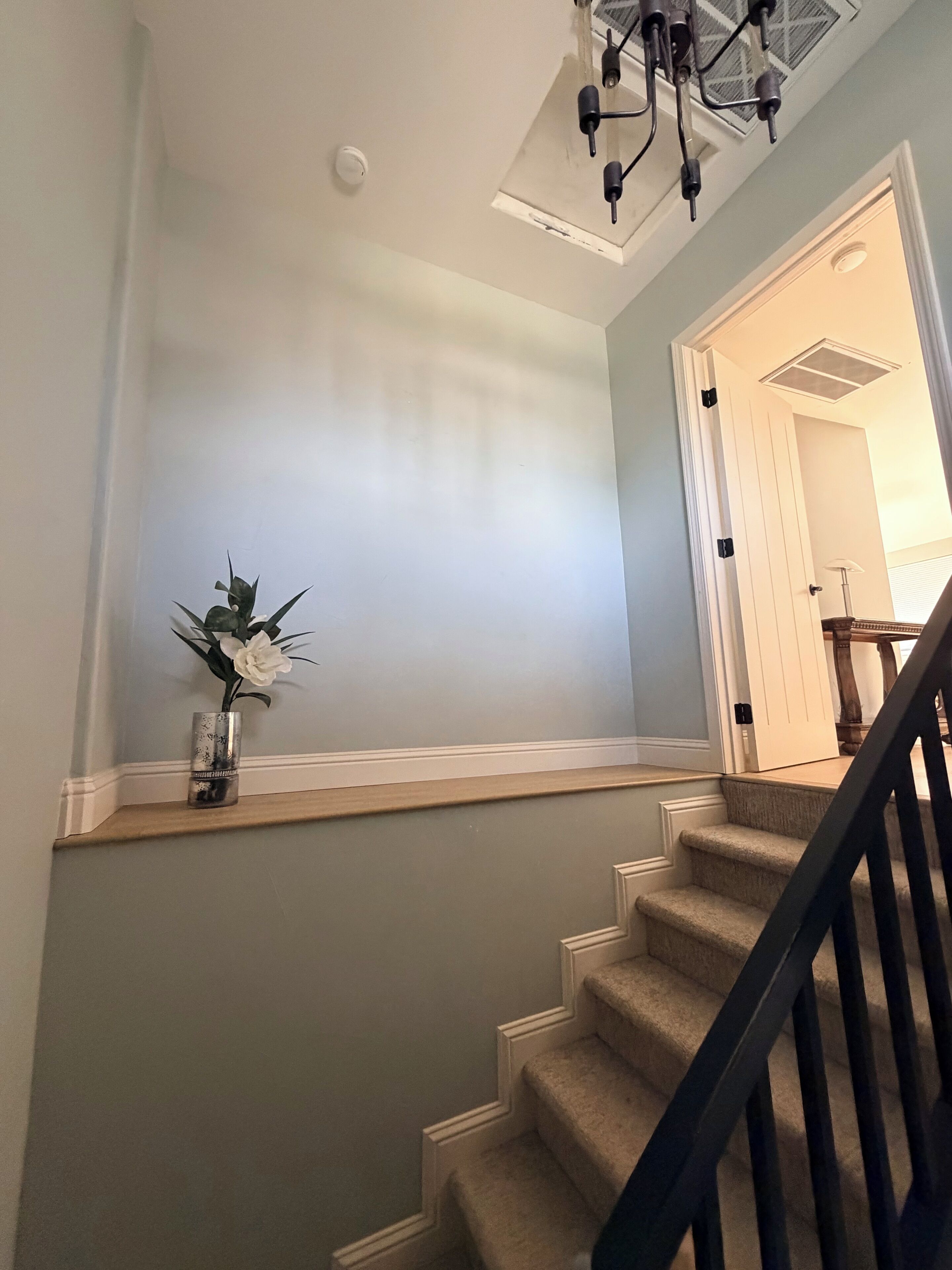 A staircase with a handrail, a wall-mounted vase with flowers, and a ceiling light fixture.
