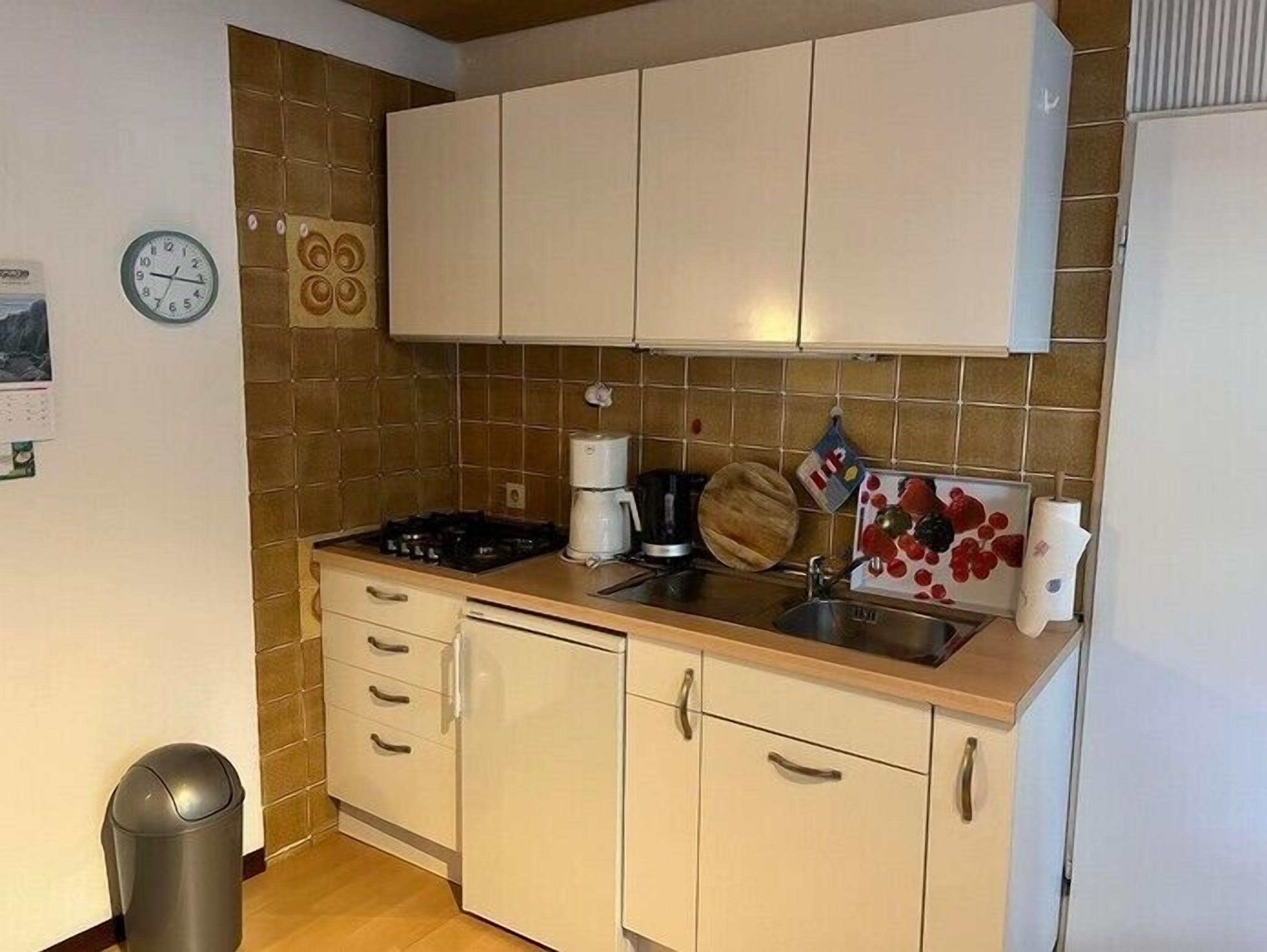 A compact kitchen with white cabinets, a stove, a coffee maker, and a sink.
