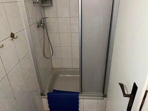 A shower area with a glass door, a handheld showerhead, and a blue towel. - Vacation apartment 2 Comfortable & fully equipped (Borkum)