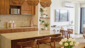 A modern kitchen with wooden cabinets, a granite countertop, and a dining area with a round table set for four. - 3 Bedroom Condo 2 Private Balconies, Pool, Gym in Downtown Cozumel. (Cozumel)