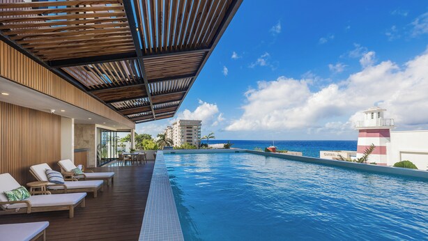 A poolside area with lounge chairs, a wooden deck, and a view of the ocean and a lighthouse. - 3 Bedroom Condo 2 Private Balconies, Pool, Gym in Downtown Cozumel. (Cozumel)