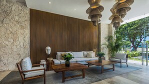 A modern lobby with a stone wall, wooden paneling, and a seating area with sofas and coffee tables. - 3 Bedroom Condo 2 Private Balconies, Pool, Gym in Downtown Cozumel. (Cozumel)