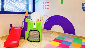 Een kinderspeelplaats met een glijbaan, een klimconstructie en een kleurrijke muur met geometrische vormen en sterren.