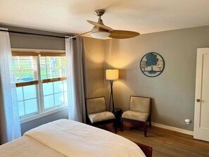 A bedroom with a bed, a ceiling fan, a window with curtains, a lamp, two chairs, and a wall decoration. - Black Walnut House @ Pioneer Park + W2 Central (Walla Walla)