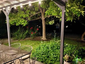 A covered outdoor area with a table and chairs, surrounded by greenery and flowering plants. - Black Walnut House @ Pioneer Park + W2 Central (Walla Walla)