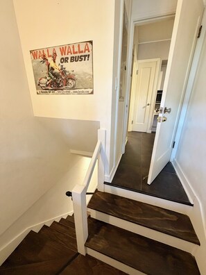 A staircase with dark wooden steps and white railings, leading to a hallway with a white door. - Black Walnut House @ Pioneer Park + W2 Central (Walla Walla)