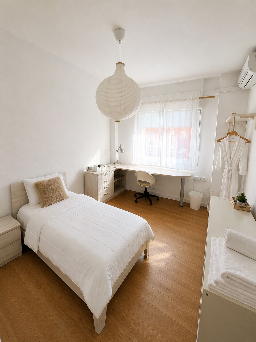A bedroom with a bed, desk, chair, and a hanging robe rack.