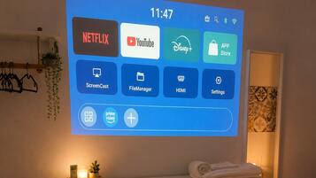 Pantalla digital en una habitación de hotel con cama, mesita de noche y estante en la pared.