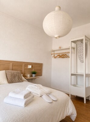 Ein Schlafzimmer mit einem Bett, einem Nachttisch mit Lampe, einer Pendelleuchte, einem Kleiderschrank und einem Wandregal.