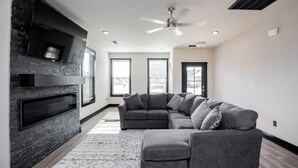 A modern living room with a sectional sofa, a fireplace, and a ceiling fan. - Minutes from the airport, beautiful new Bentonville home! (Bentonville)