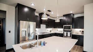 A modern kitchen with dark cabinetry, stainless steel appliances, and pendant lighting. - Minutes from the airport, beautiful new Bentonville home! (Bentonville)