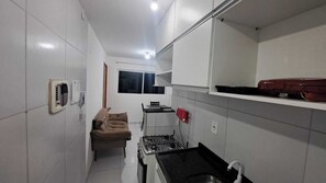 Una cocina compacta con paredes de azulejos blancos, una estufa a gas, una pequeña mesa de comedor y un sofá.