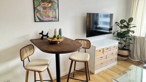 Una sala moderna con una mesa redonda para comer, dos sillas, un televisor de pantalla plana, una planta grande en maceta y una obra de arte colgada en la pared.