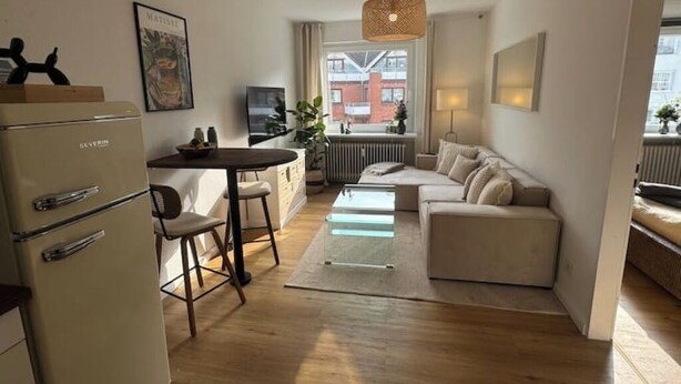 Un espacio habitable compacto con kitchenette, un sofá, una mesa de comedor y una lámpara colgante.