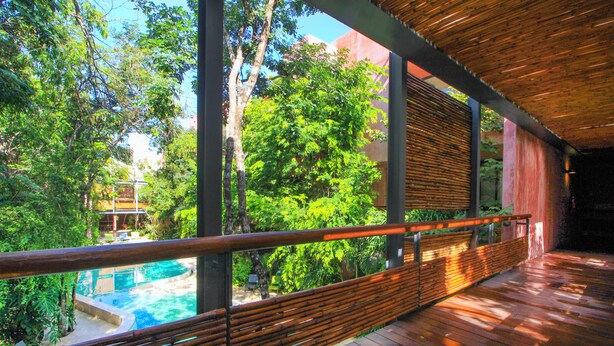 A wooden deck with a view of a swimming pool and lush greenery. - Mi Querido Tulum Apt with Pool-View (Tulum)