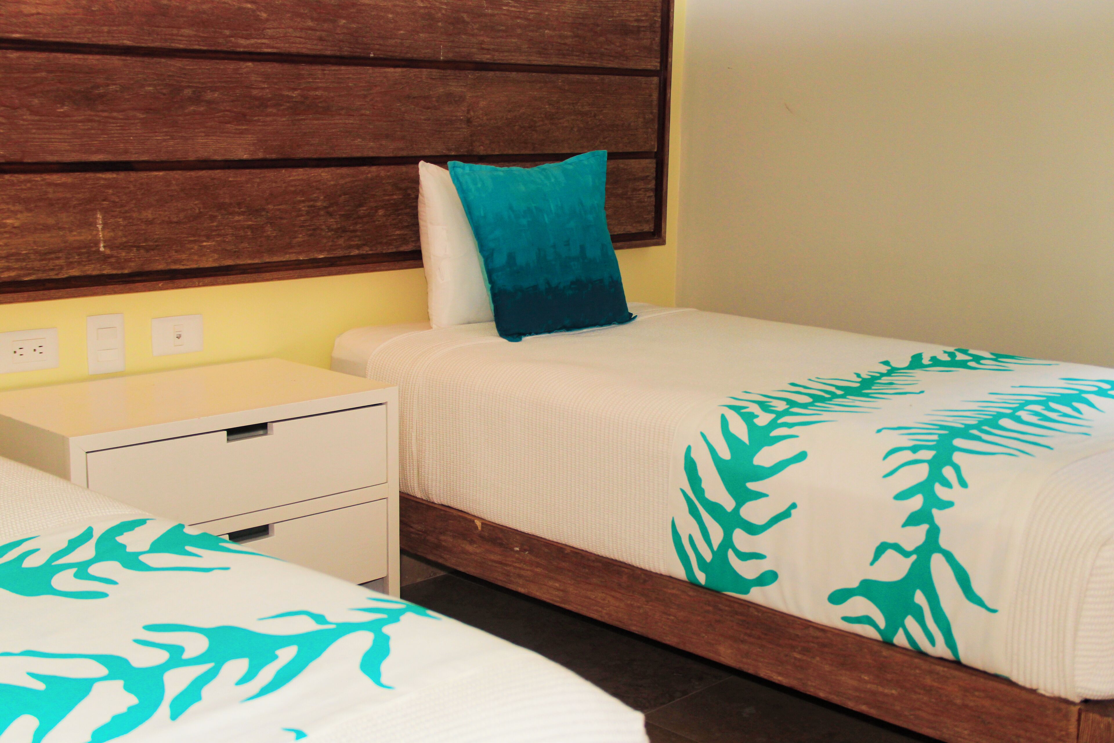 A hotel room with two single beds, a wooden headboard, a nightstand, and a white drawer unit.