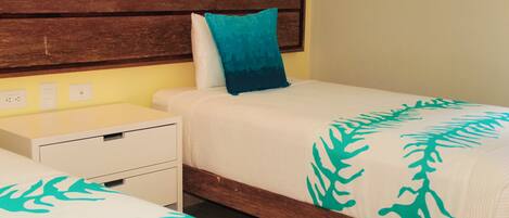 A hotel room with two single beds, a wooden headboard, a nightstand, and a white drawer unit.
